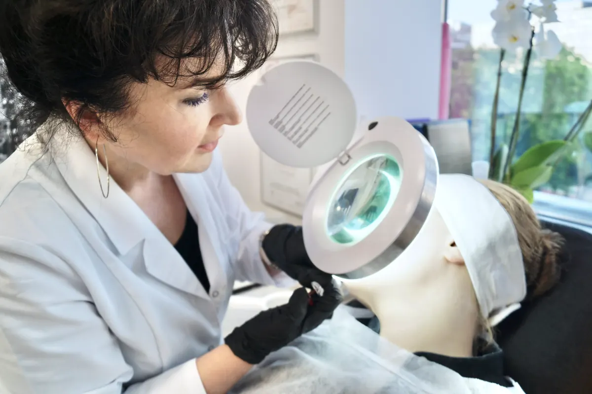 Dr Dorota Nawacka ogląda skórę pacjentki przez lampę z lupą w gabinecie.