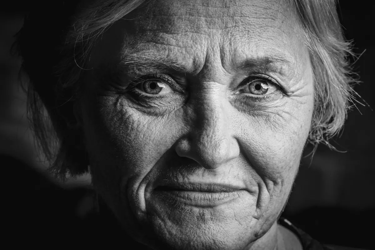 Czarno-białe zdjęcie starszej kobiety w zbliżeniu, ze zmarszczkami wokół oczu.